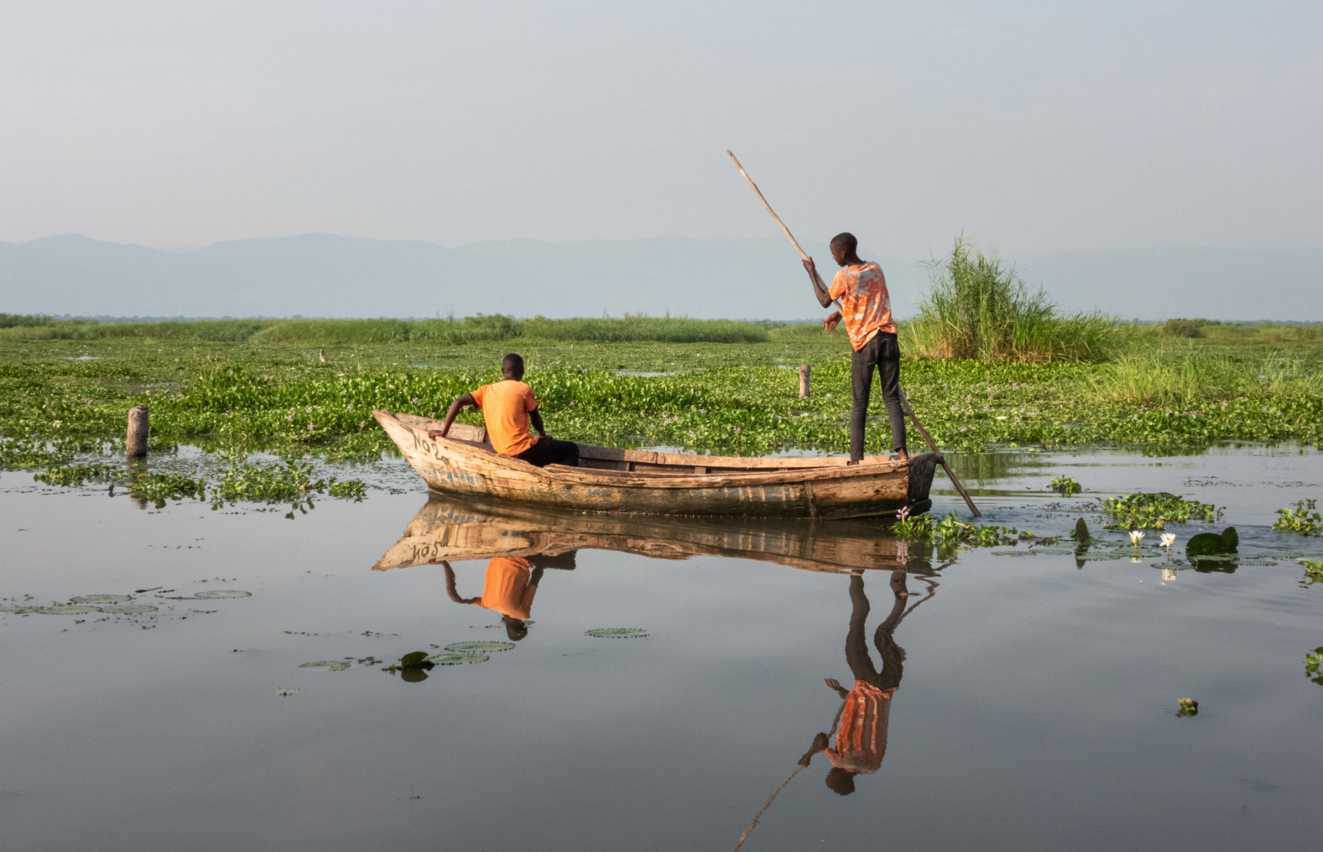 Two local boatmen poling a wooden canoe through the wetlands